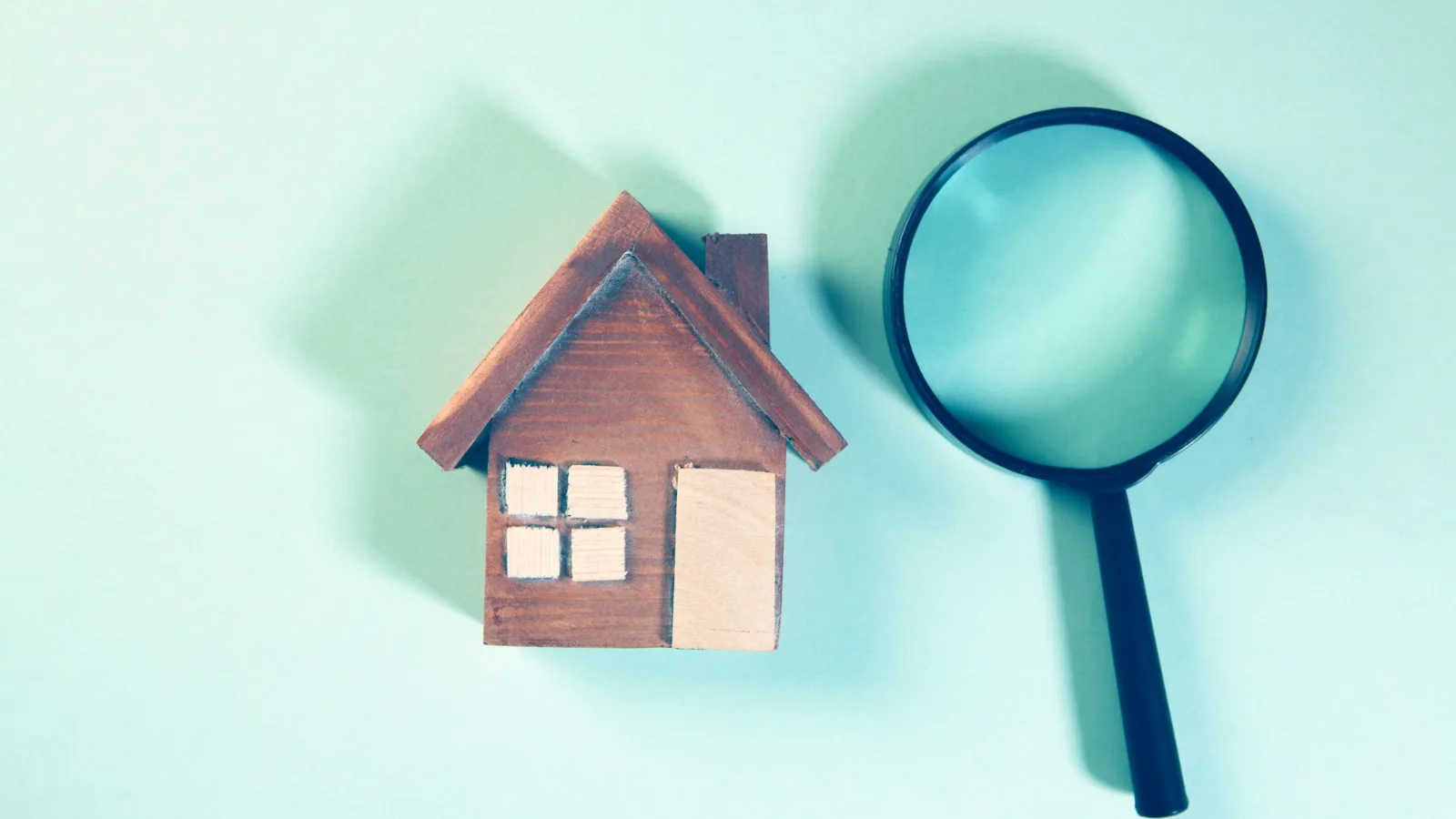 Magnifying glass beside a small wooden house, for an article on the cost of mold inspection